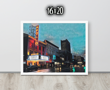Framed artwork of a cityscape with The Apollo Theatre at night, displayed on a white wooden surface.