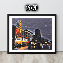Framed artwork of a cityscape with The Apollo Theatre at night, displayed on a black wooden surface.