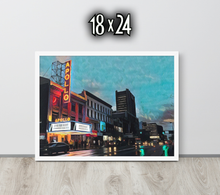Framed artwork 18 x 24 of a cityscape with The Apollo Theatre at night, displayed on a black wooden surface.