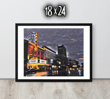 Framed artwork of a cityscape with The Apollo Theatre at night, displayed on a black wooden surface.